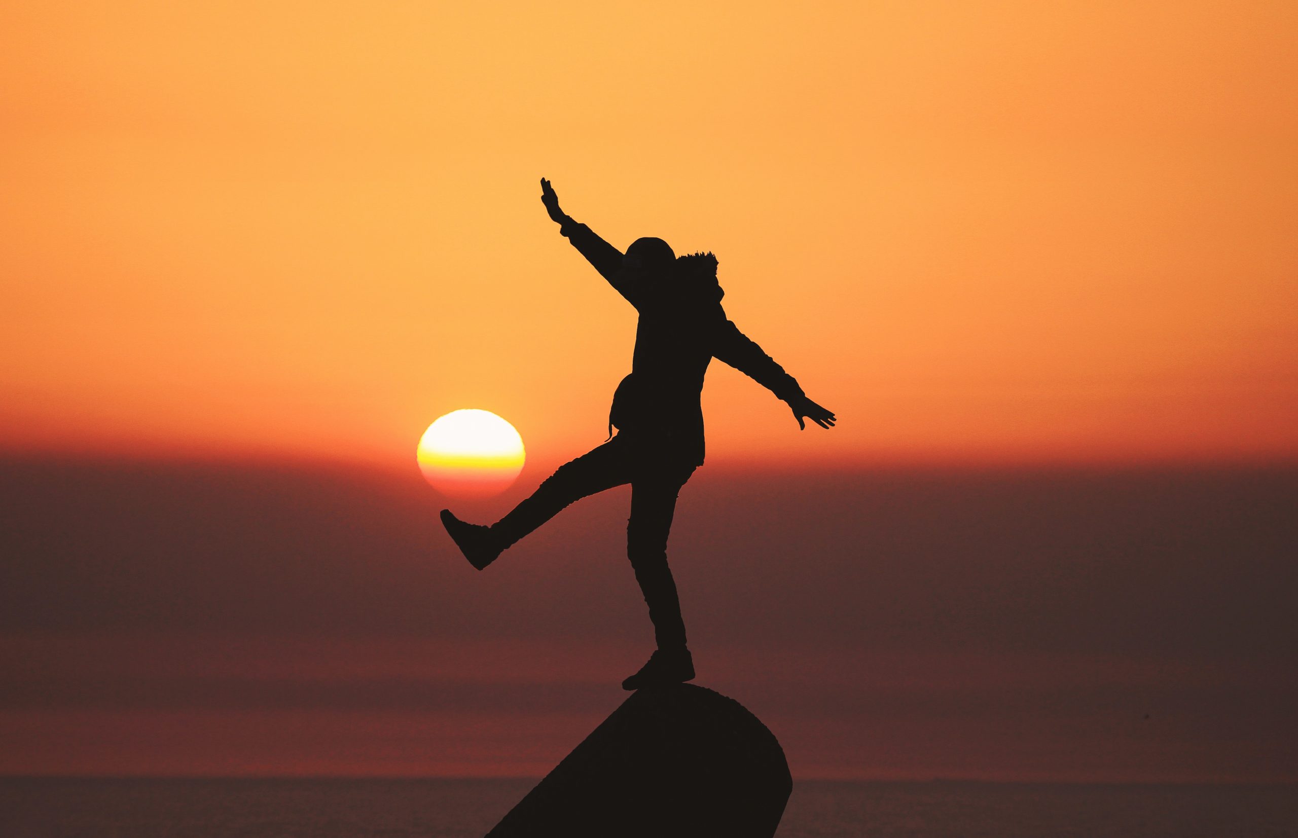 person balancing on rock in sunset